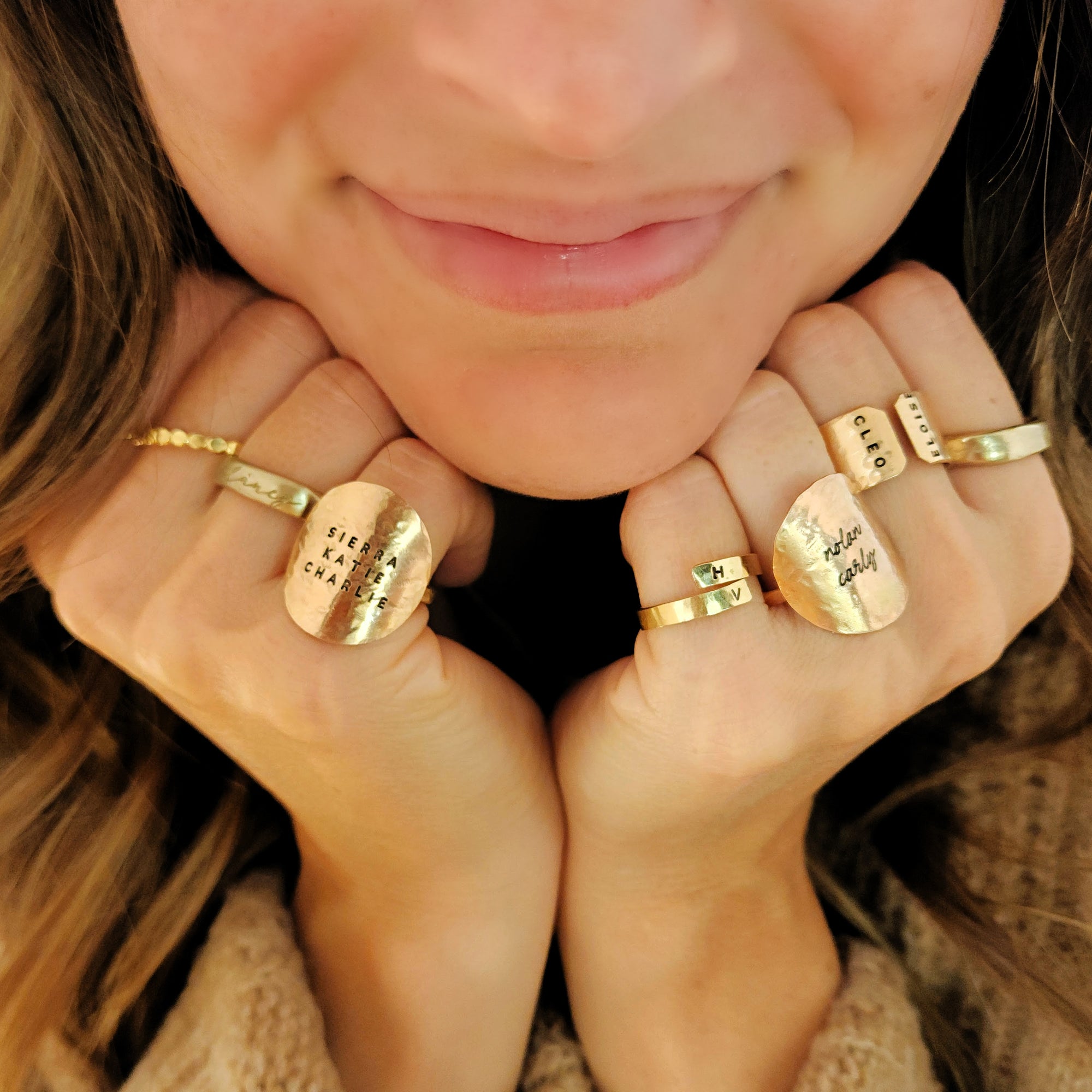 Close-up of a person wearing multiple gold rings with engraved text on their fingers.
