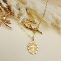 Gold necklace with a cross pendant on a soft beige background