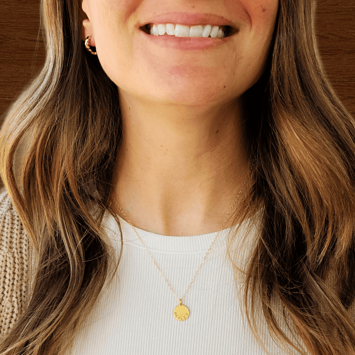 Close-up of a woman wearing a gold necklace with a pendant, smiling.