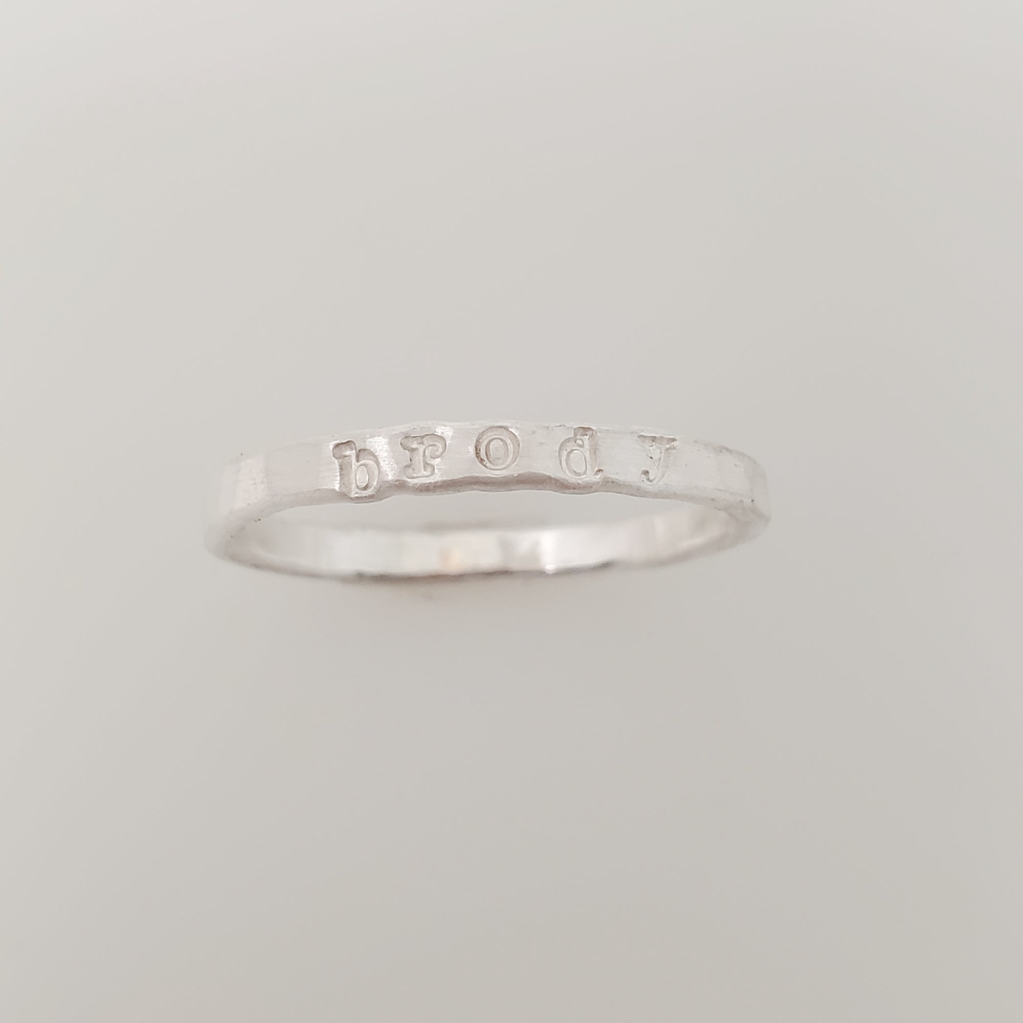 A silver stacking name ring with the name 'brody' hand-stamped on it.