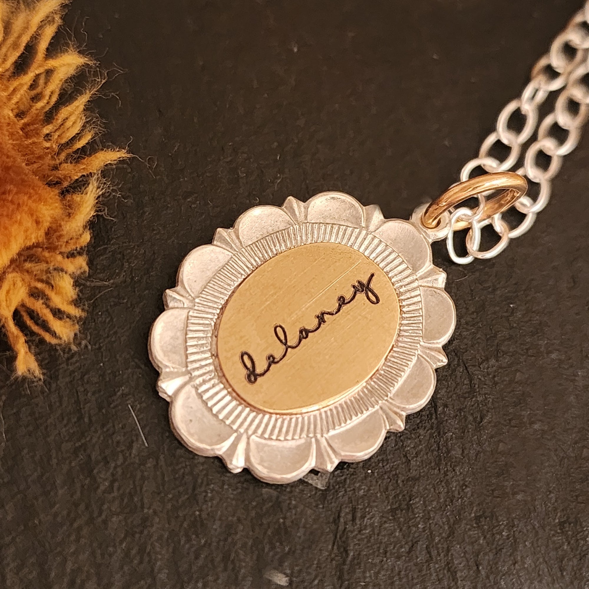 Gold and silver necklace with a floral pendant on a dark surface