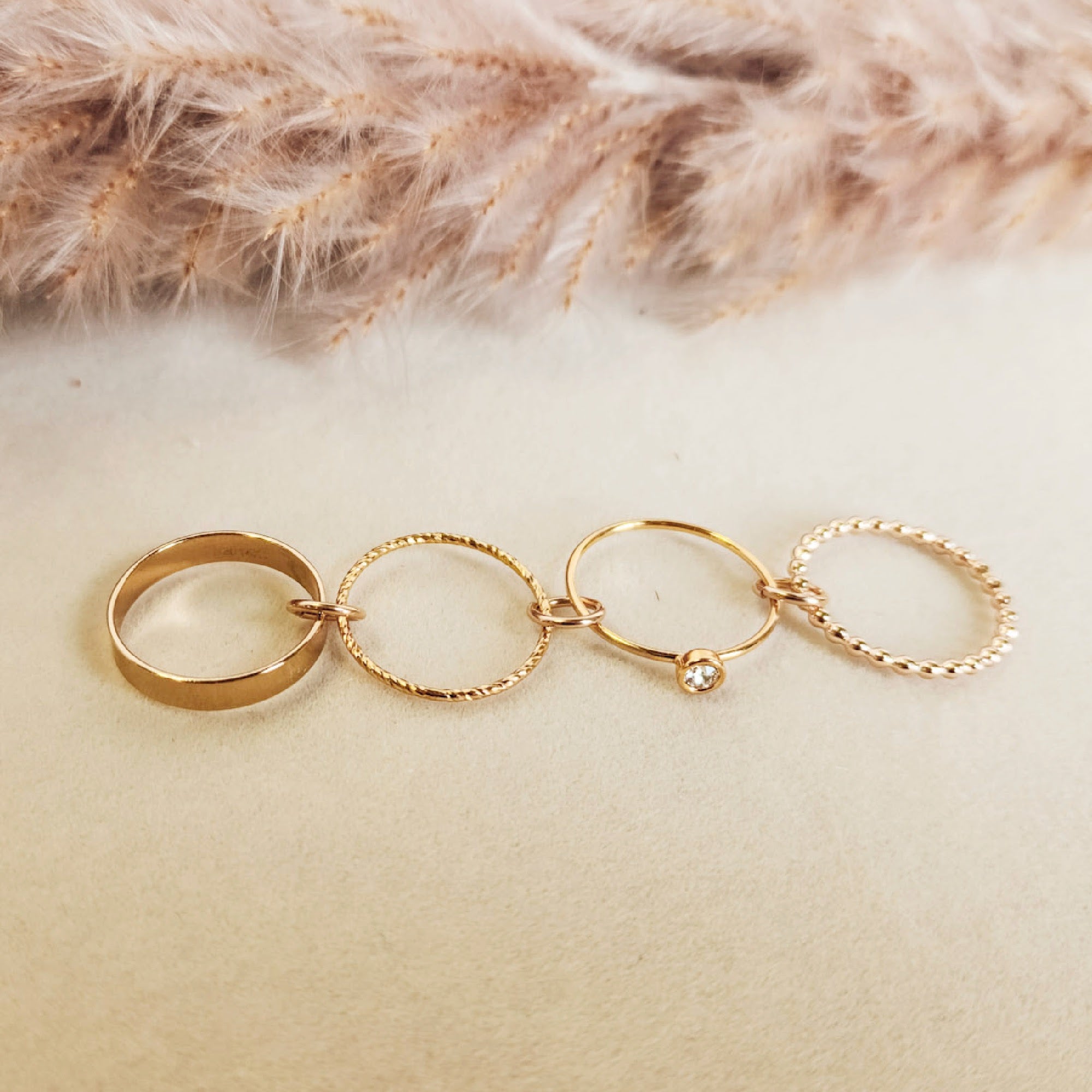 Set of gold rings on a soft beige surface with pampas grass in the background