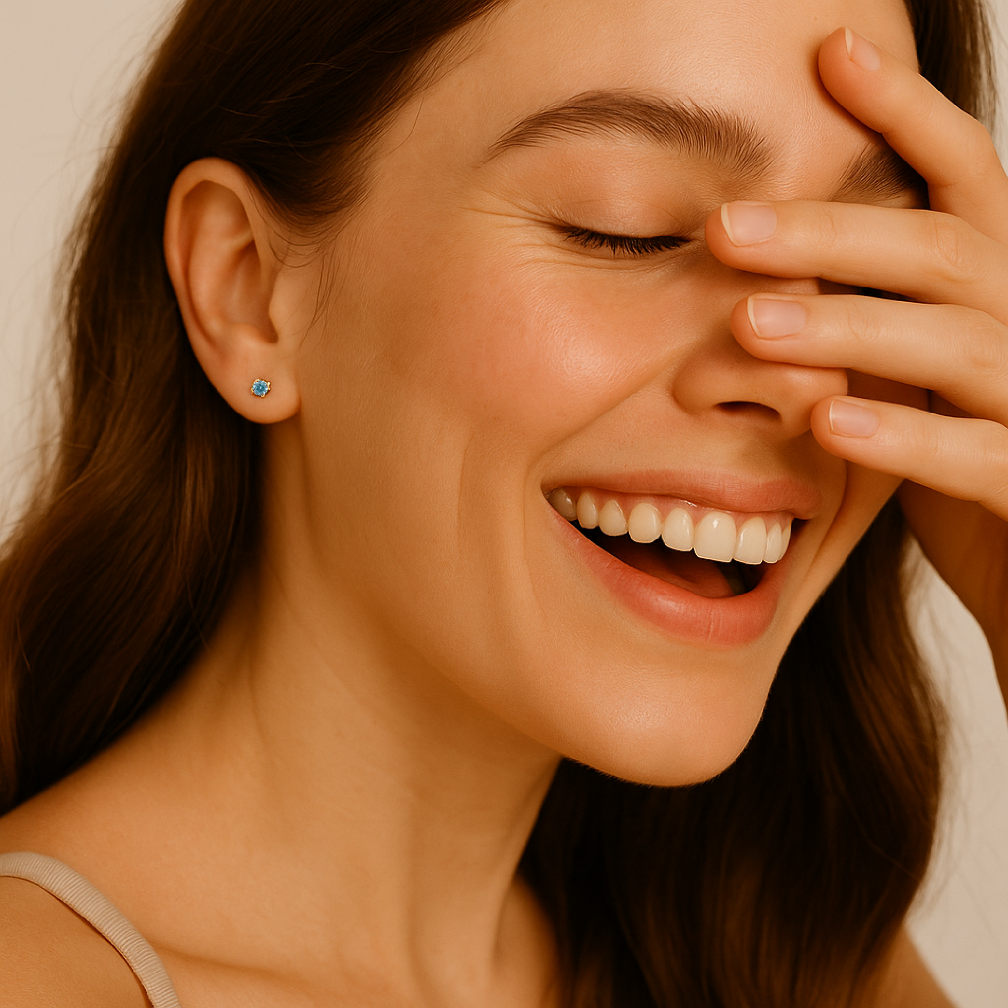 Woman with a bright smile covering her eyes with her hand, wearing a white top.