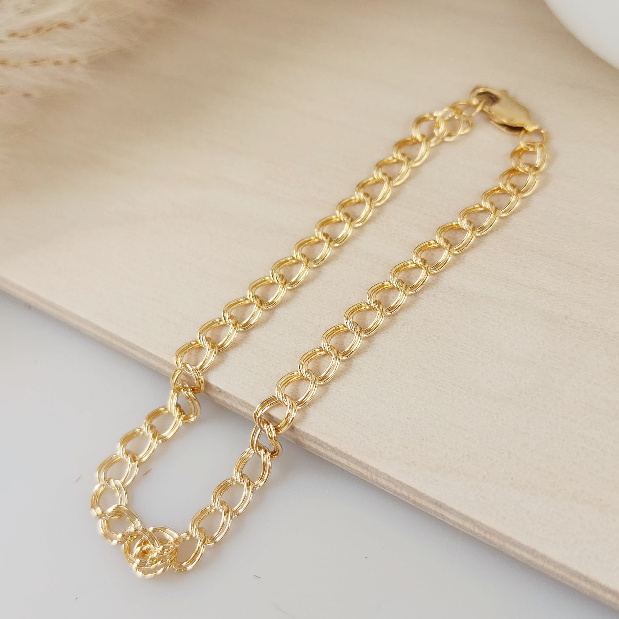 A gold double cable chain bracelet resting on a beige surface.