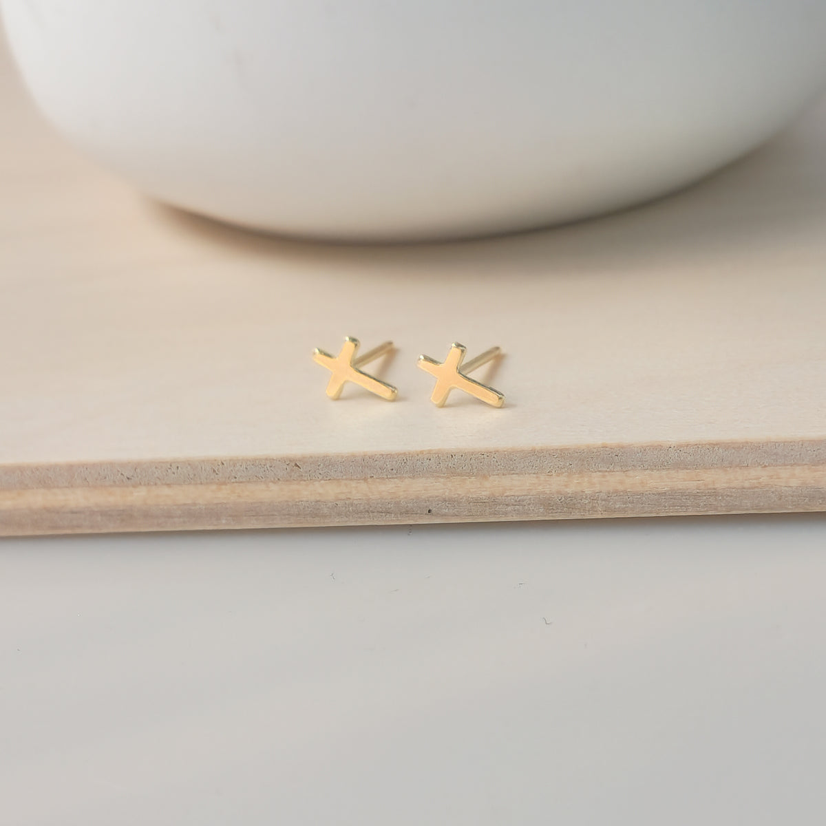 A pair of dainty gold-filled cross stud earrings placed on a wooden surface.