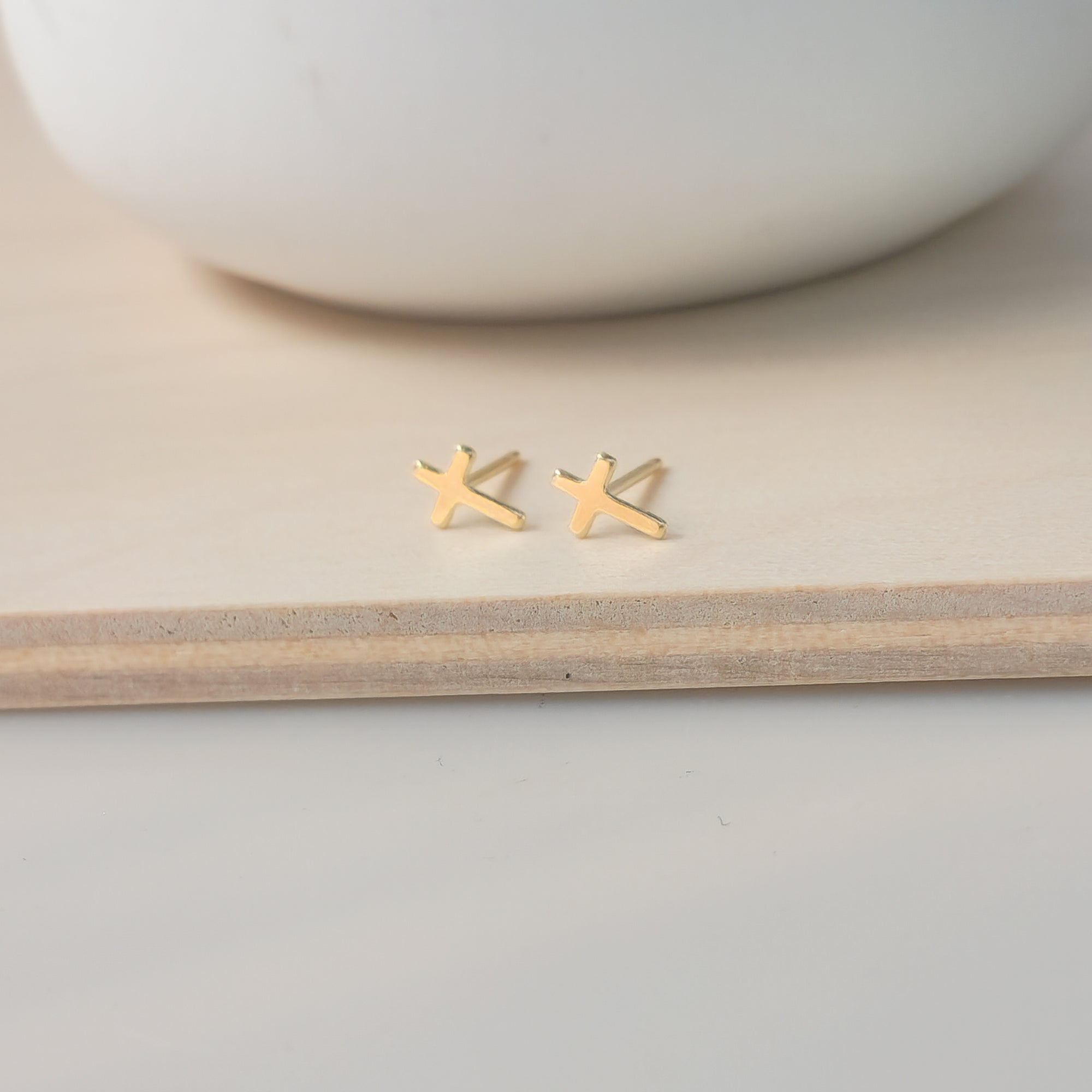 A pair of dainty gold-filled cross stud earrings placed on a wooden surface.