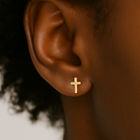 Gold cross earring on a person's ear with a blurred background