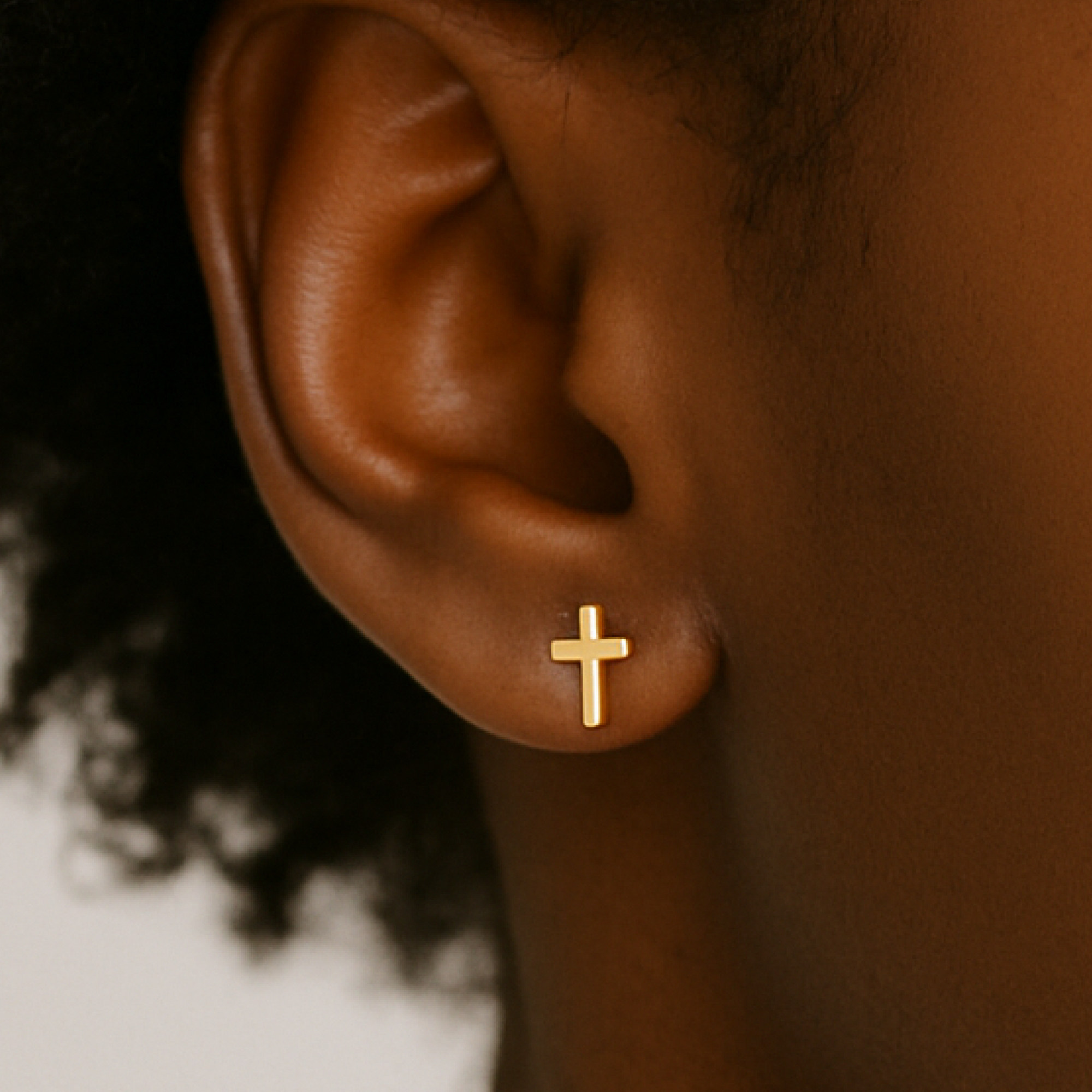 Gold cross earring on a person's ear with a blurred background