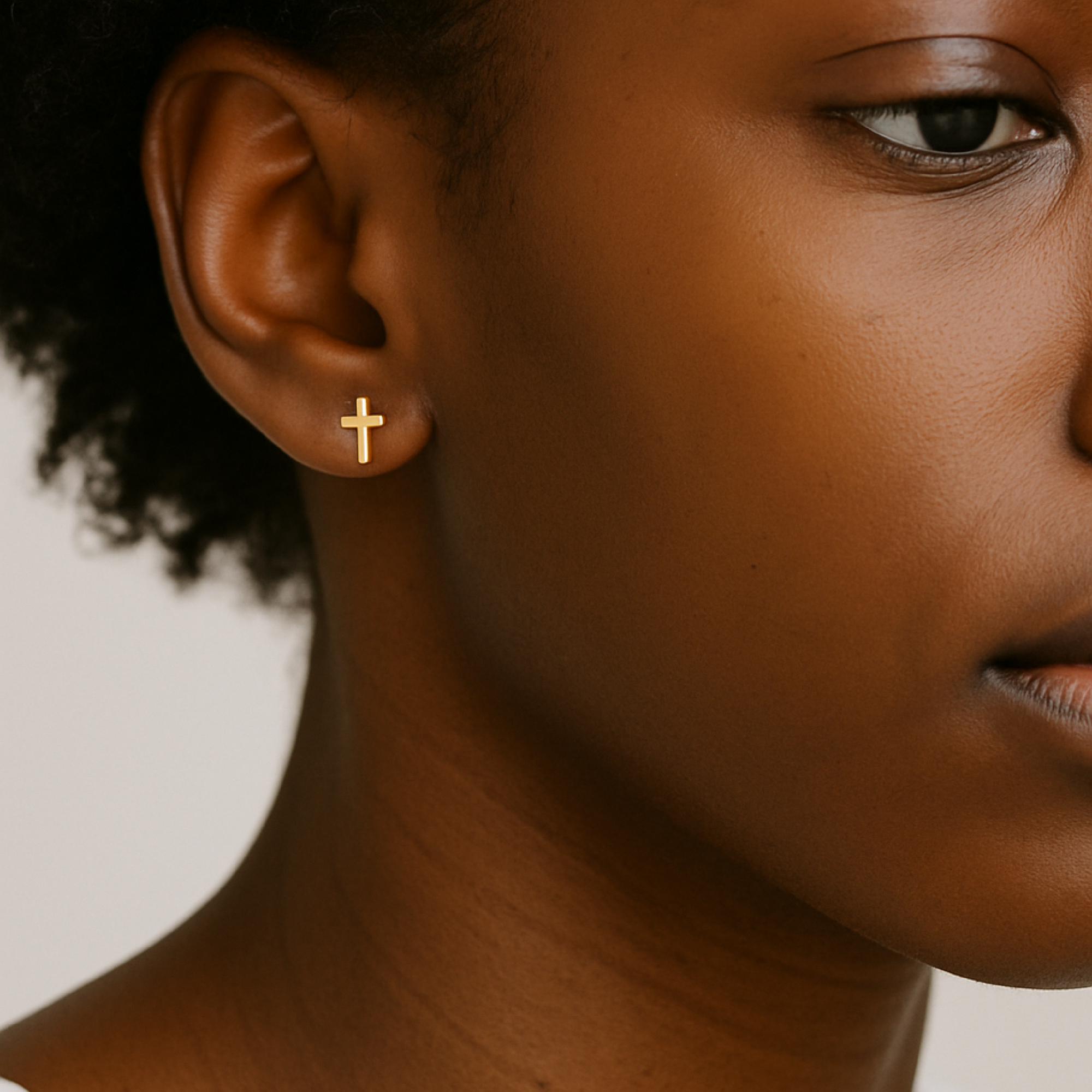 Close-up of a person wearing a gold cross earring against a neutral background