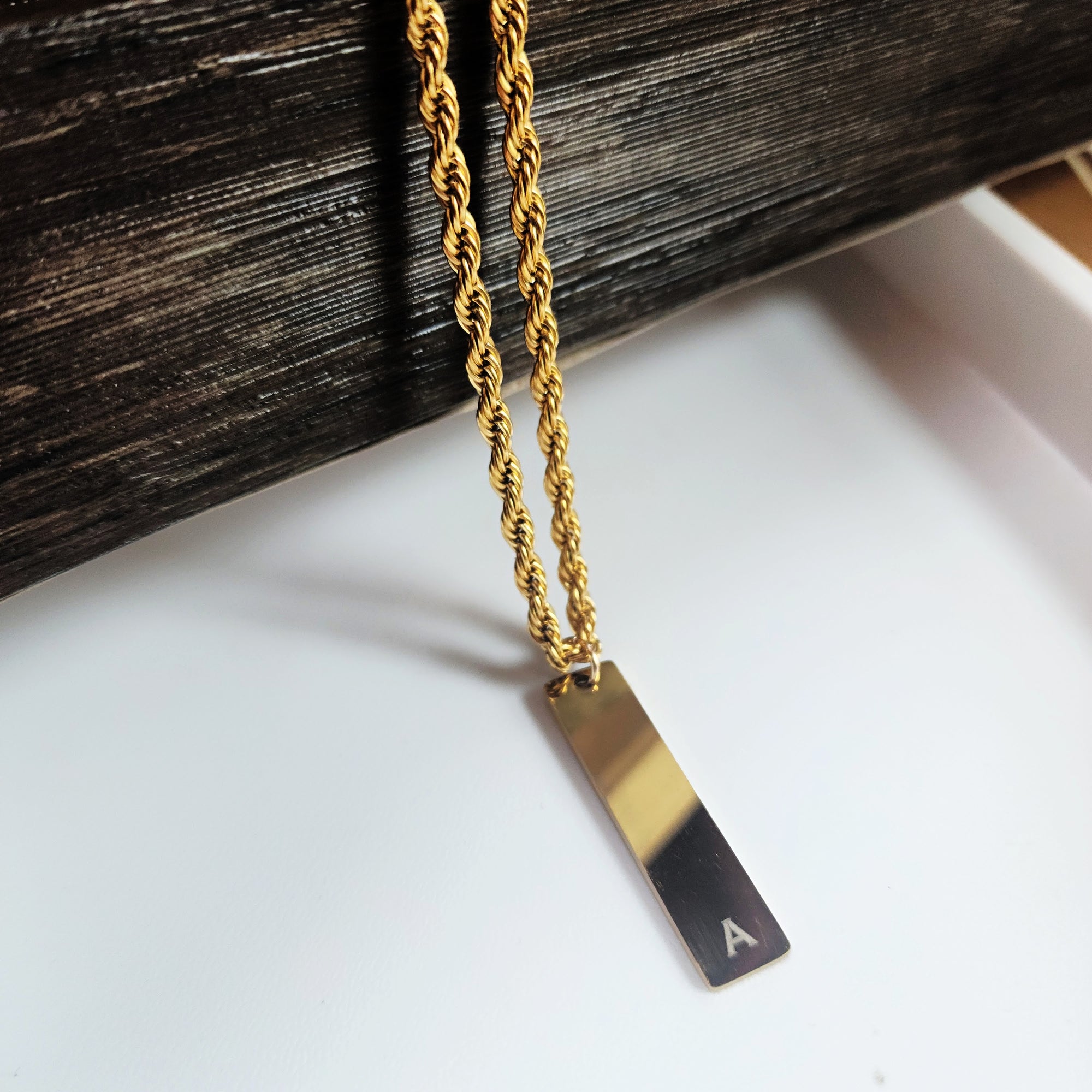 Gold necklace with a rectangular pendant on a white surface