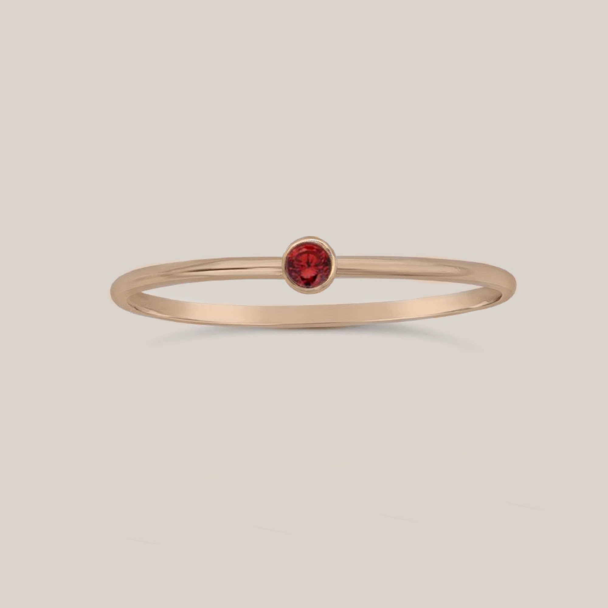 A gold-filled band ring with a red garnet crystal accent, intended for stacking.