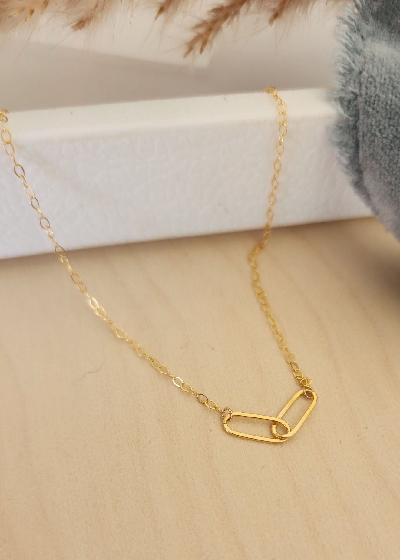 A 14k gold filled cable chain necklace with two larger oval links displayed on a white surface, alongside a grey cloth.