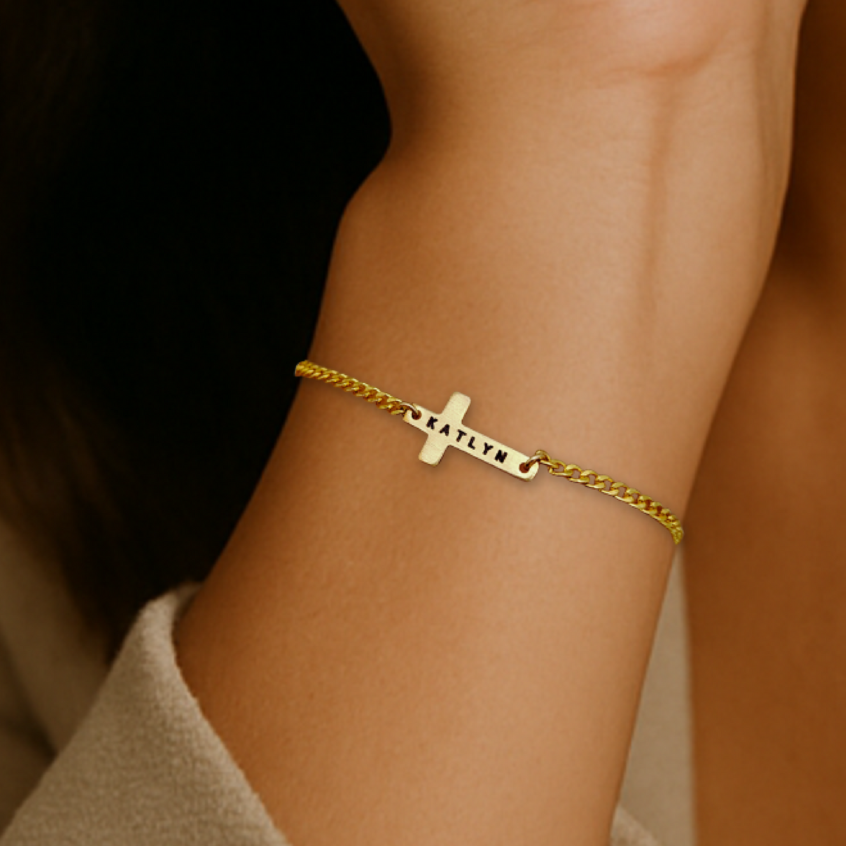 Gold bracelet with a cross charm on a wrist against a neutral background