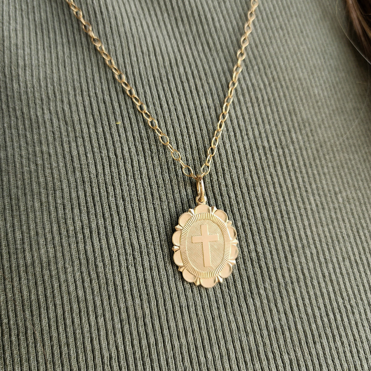 Gold necklace with a cross pendant on a textured green surface