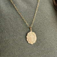 Gold necklace with a cross pendant on a textured green surface