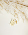 Minimal gold date necklace and angel wing charm displayed on cream textured surface