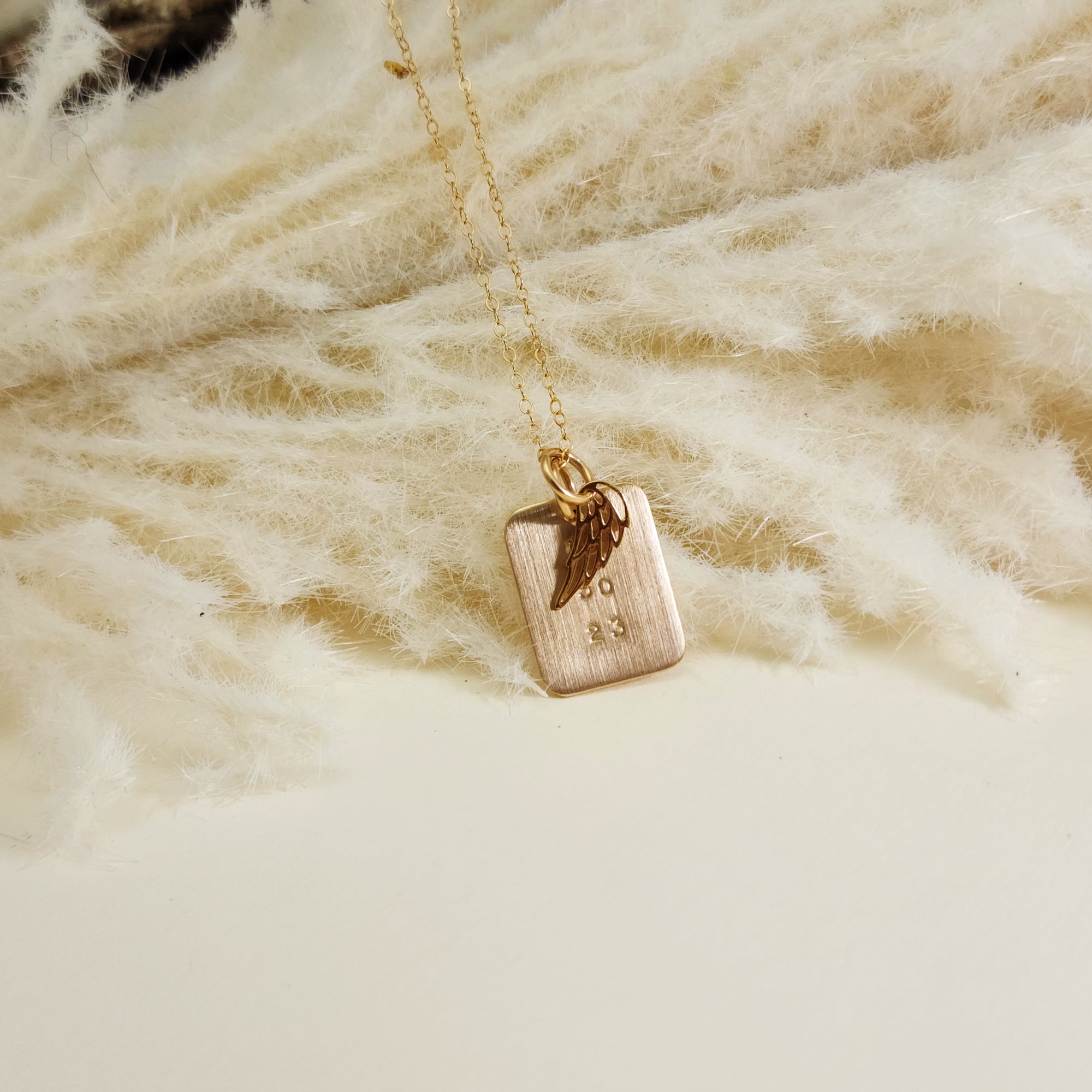 Gold date necklace with angel wing charm resting on fluffy cream fabric