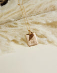 Gold date necklace with angel wing charm resting on fluffy cream fabric