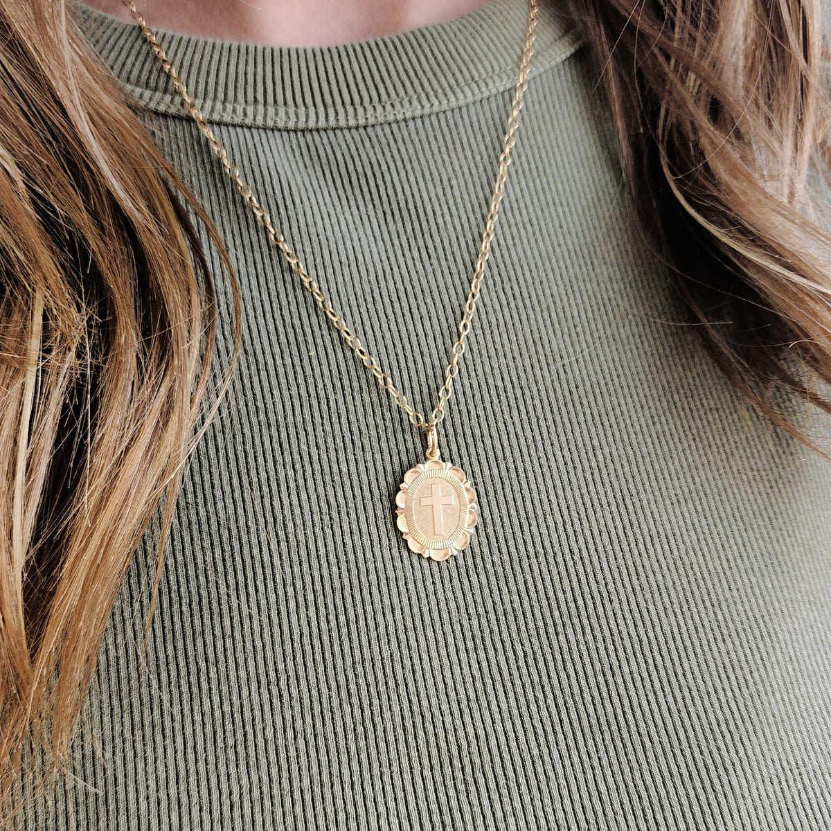 Gold necklace with a pendant on a person wearing a green ribbed sweater