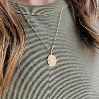 Gold necklace with a pendant on a person wearing a green ribbed sweater
