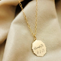 Gold necklace with a engraved pendant on a beige fabric background