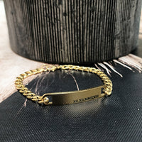 Gold chain bracelet with engraved text on a black textured surface