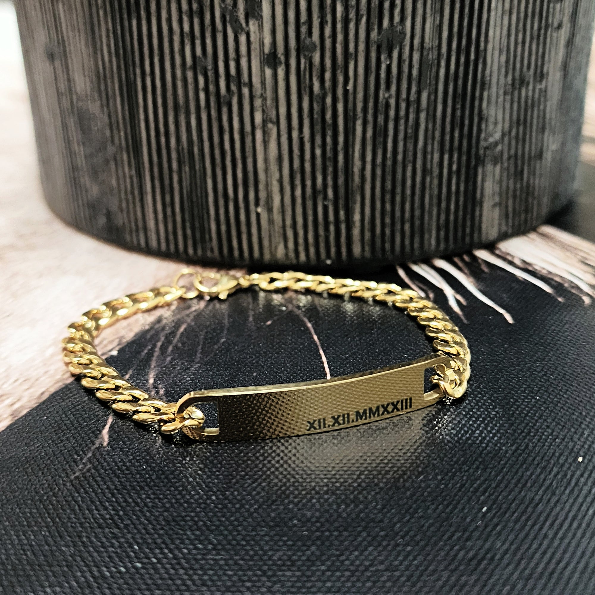 Gold chain bracelet with engraved text on a black textured surface
