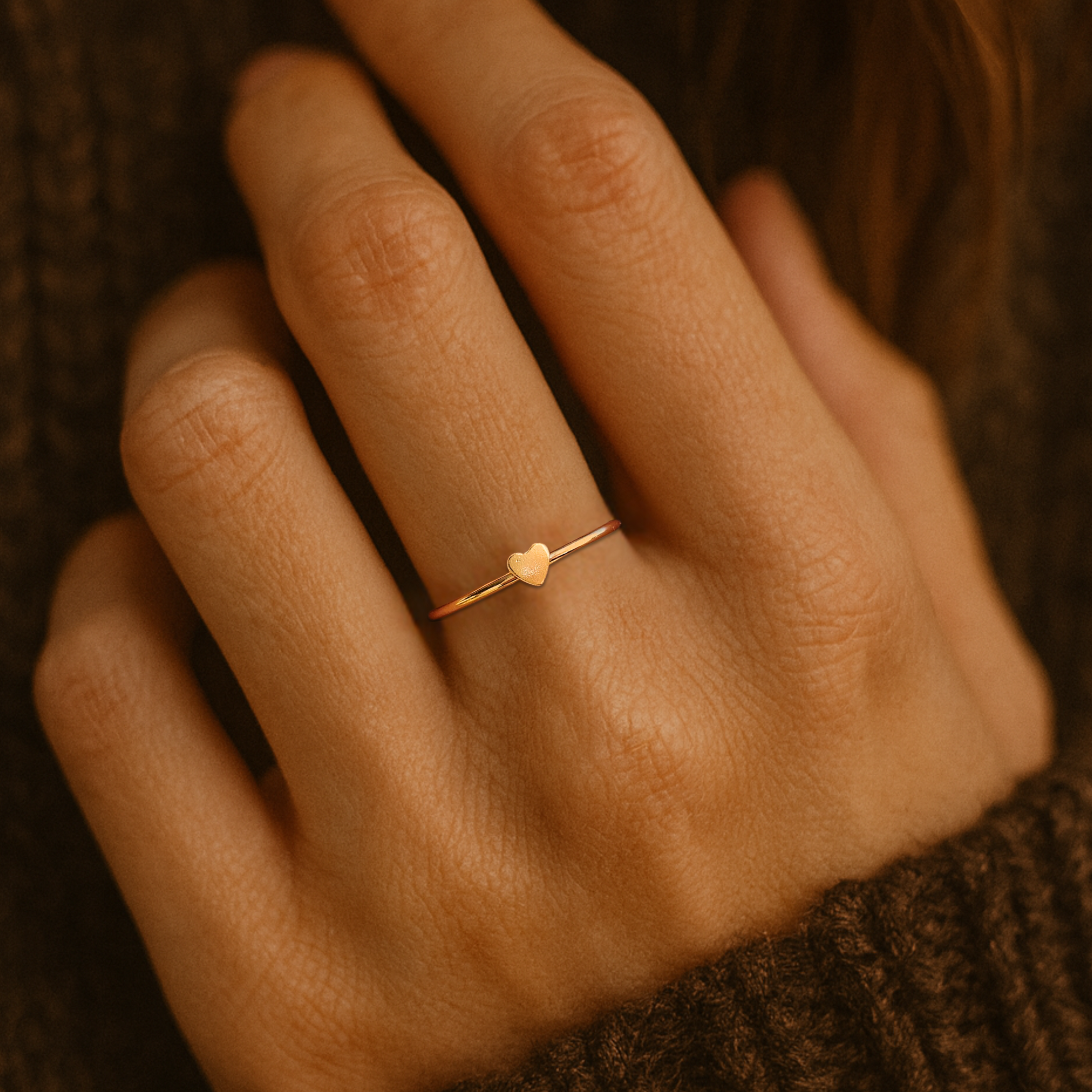 Gold ring with a heart-shaped center on a person's finger against a brown background