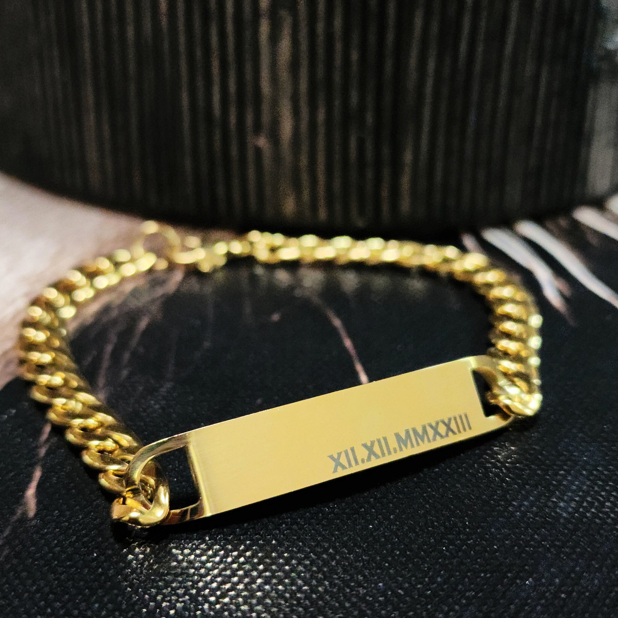 Gold chain bracelet with a engraved tag on a black textured surface