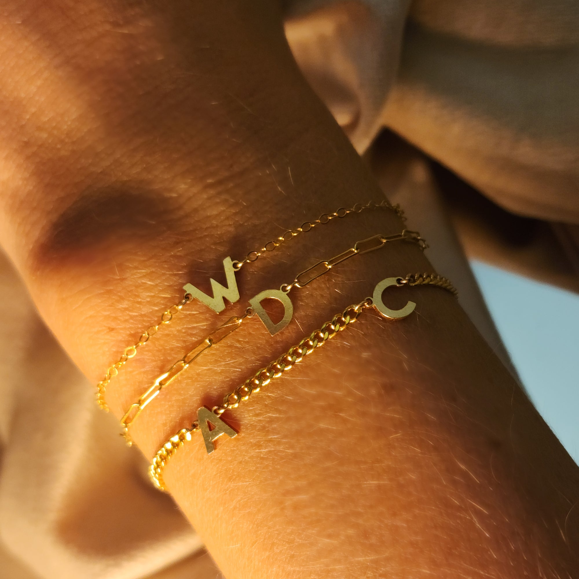 Gold bracelets with letter charms on a wrist