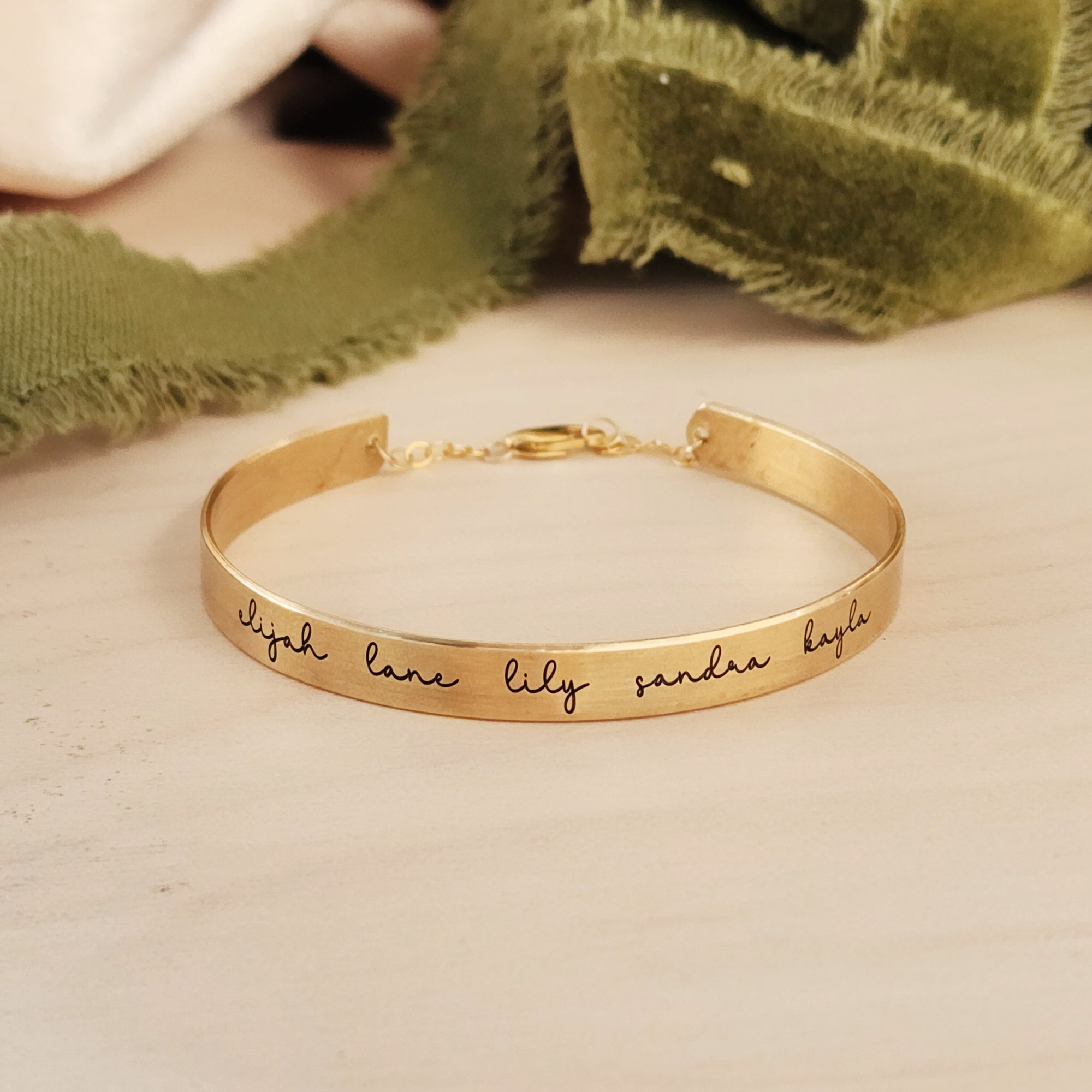A gold-colored cuff bracelet with custom names engraved on it