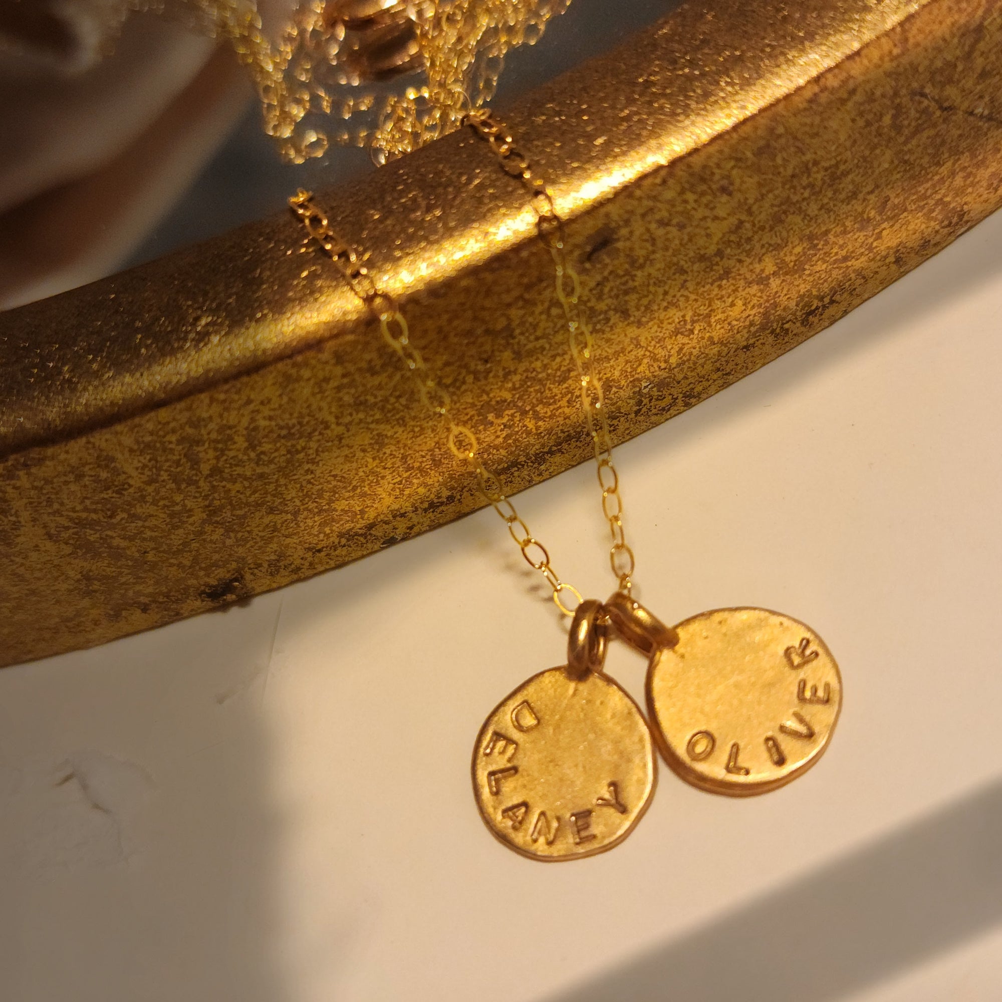 Gold necklace with two engraved pendants on a reflective surface