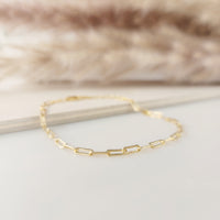 A gold-filled paperclip bracelet laid out on a flat surface with a furry object in the background.