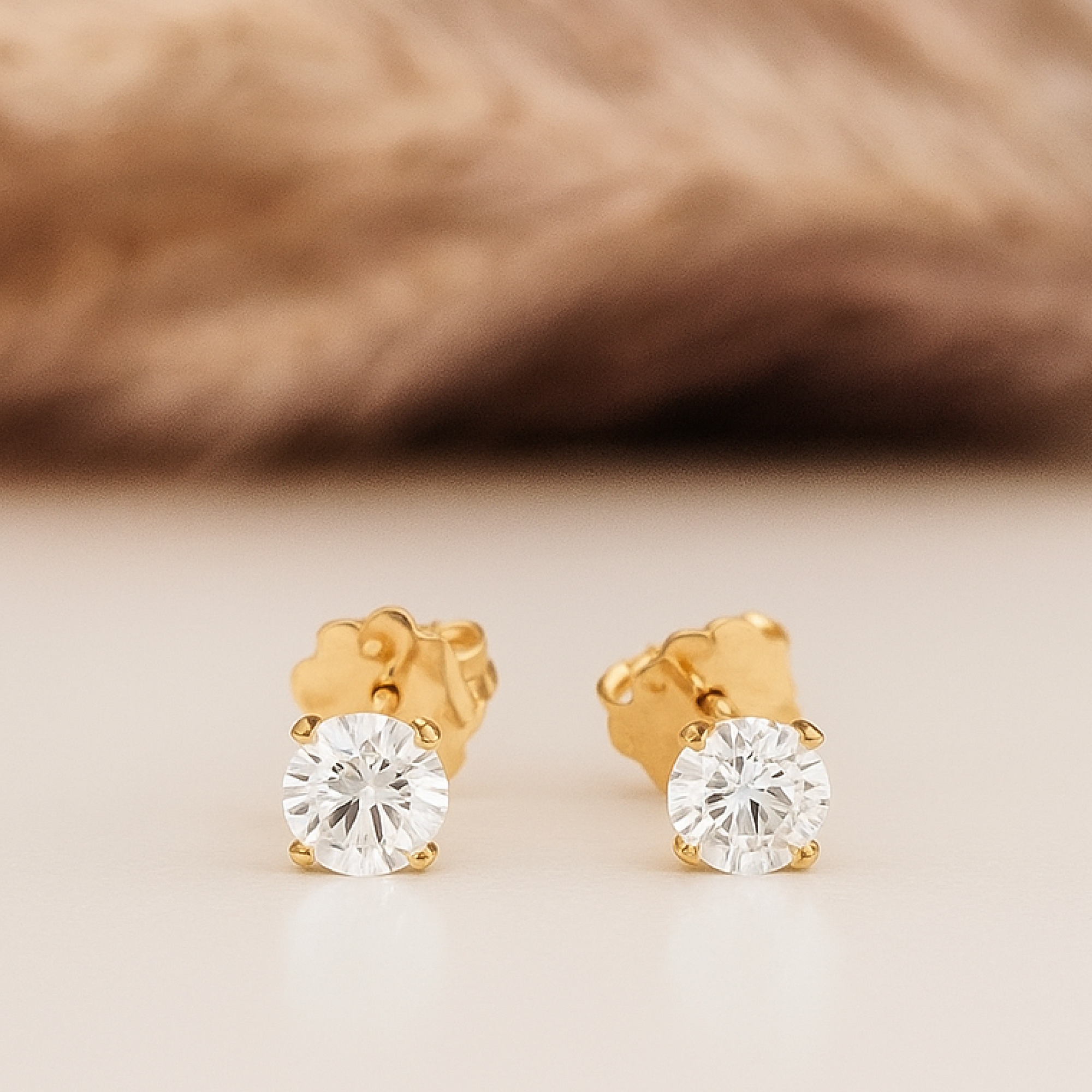 Gold stud earrings with clear gemstones on a beige background