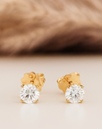 Gold stud earrings with clear gemstones on a beige background