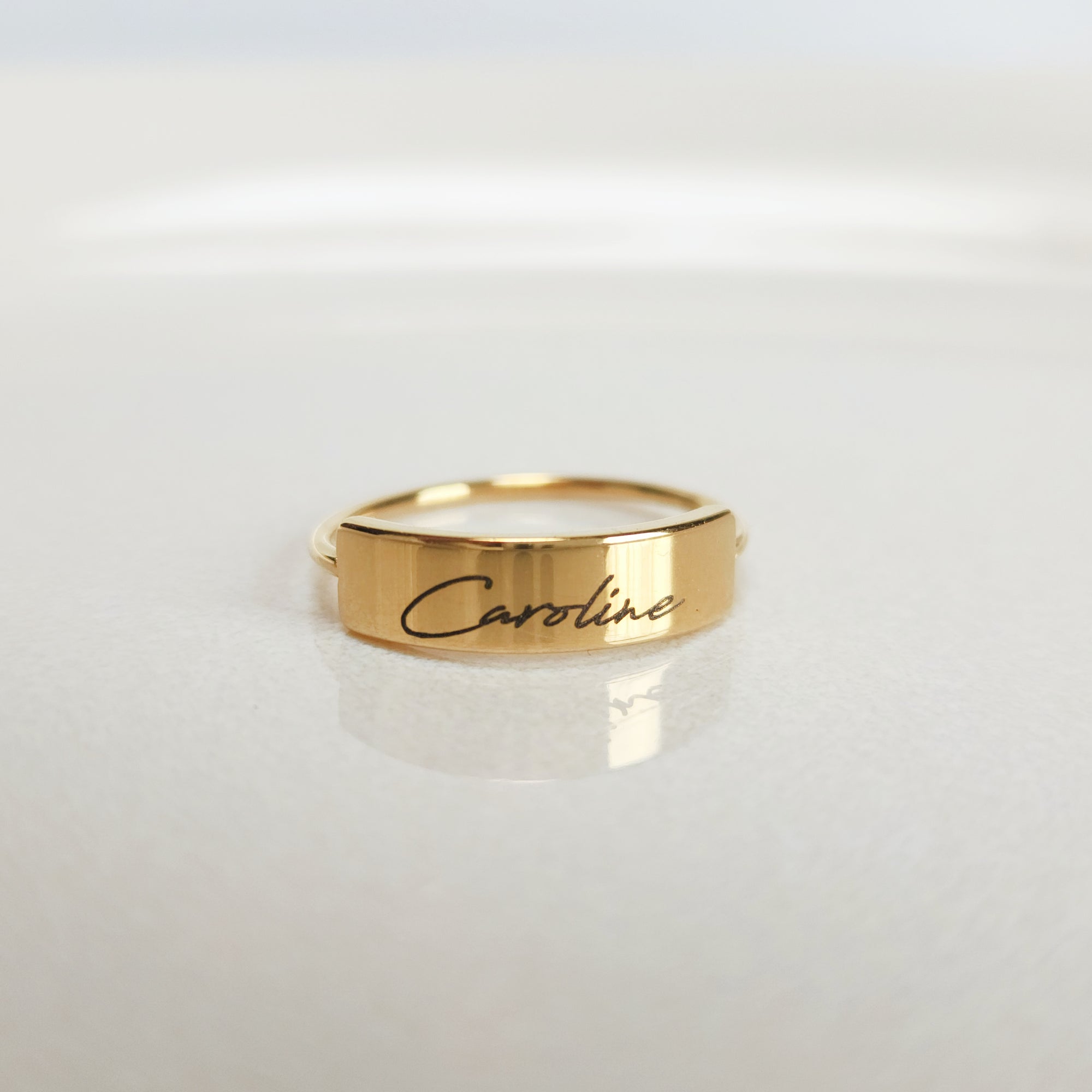 A gold-colored ring with the name 'Caroline' engraved on it, displayed on a white surface.