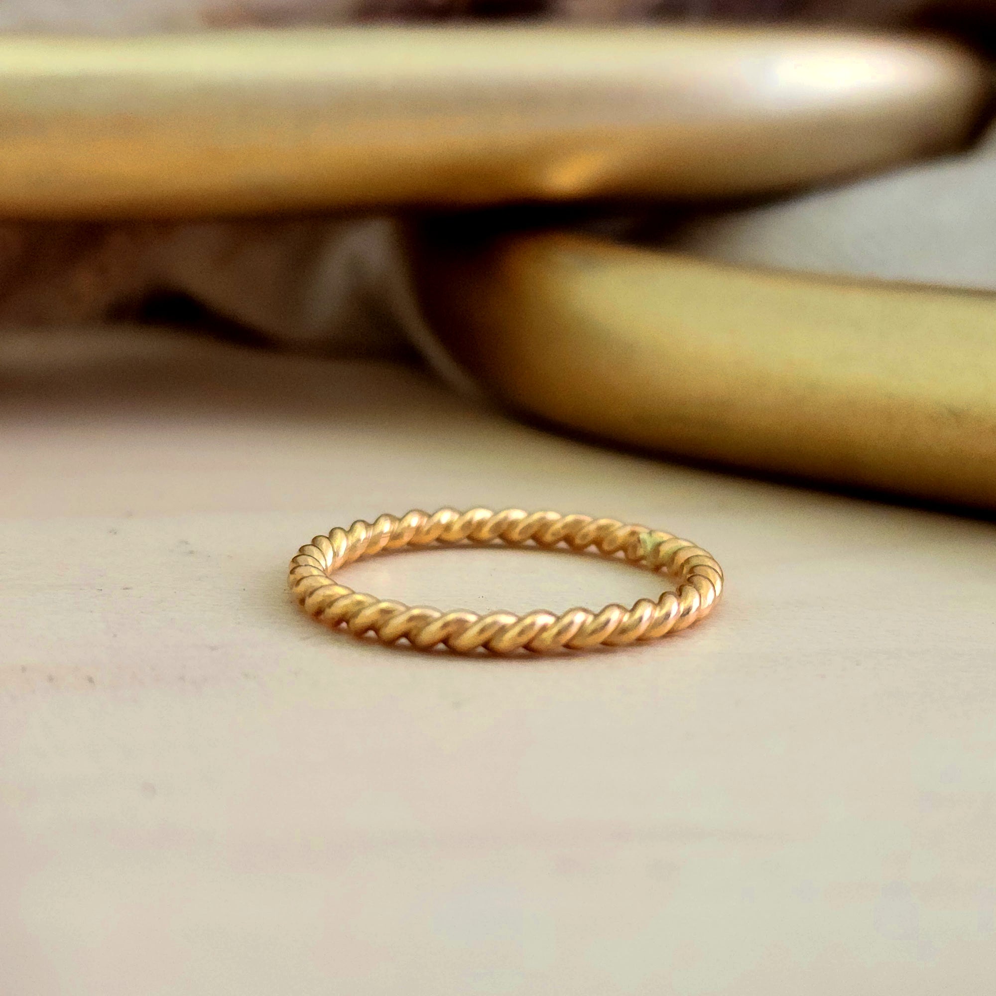 A thin twisted gold stacking ring displayed on a surface.