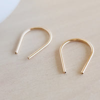 Close-up of minimalist gold U-shaped earrings on light wood background