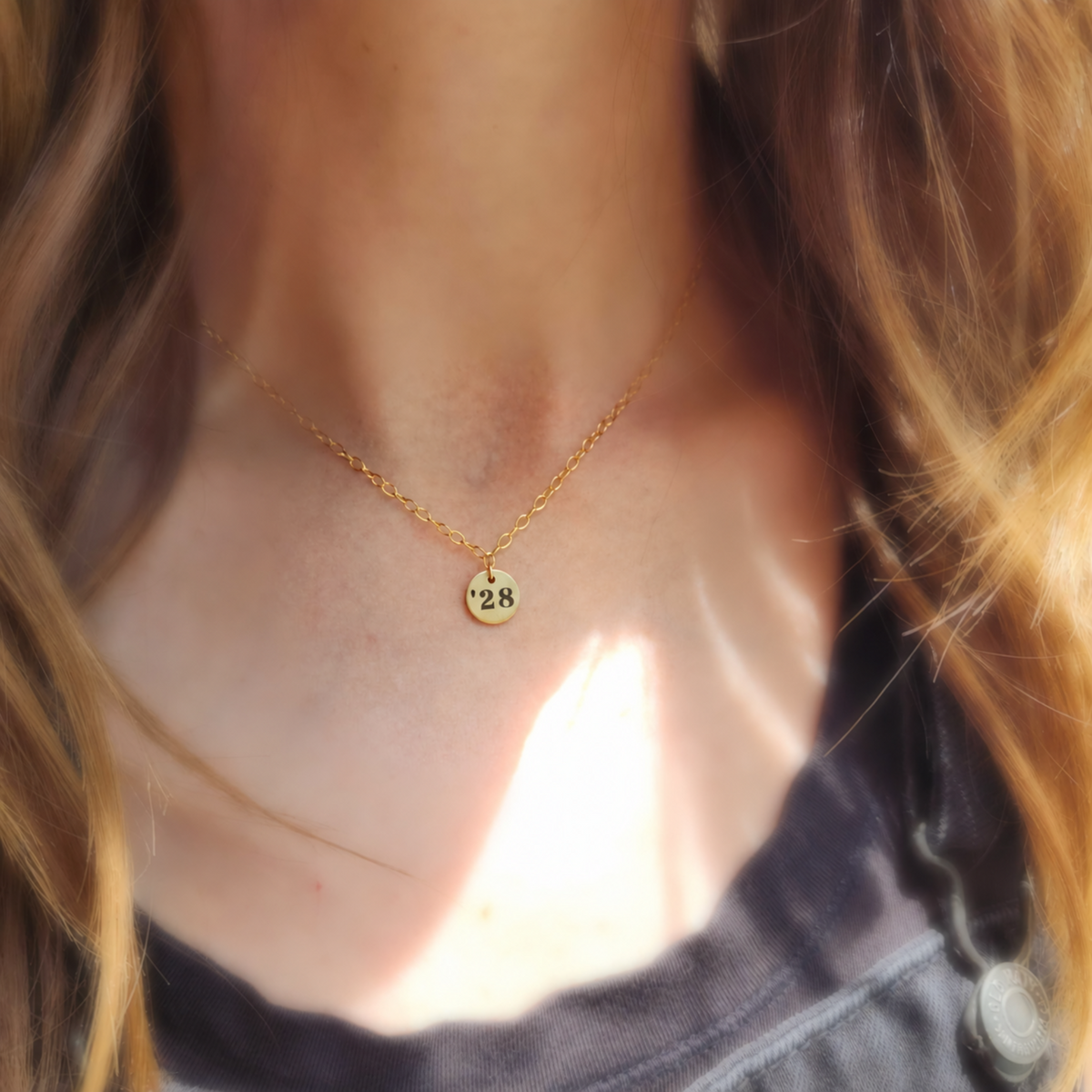 small round pendant necklace gold on a cable chain that says '28 on a persons neck