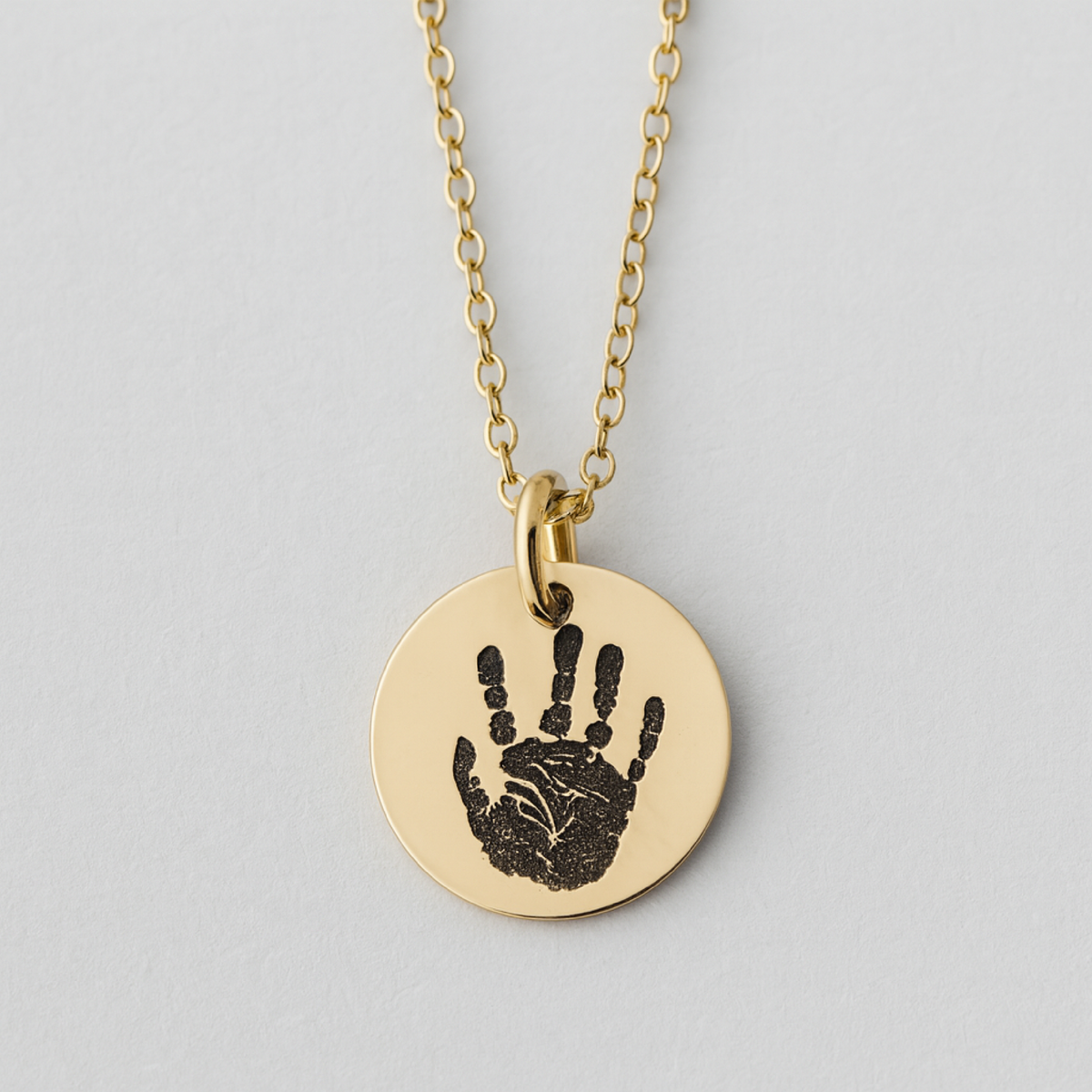 Gold necklace with a round pendant featuring a handprint on a light gray background