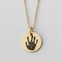 Gold necklace with a round pendant featuring a handprint on a light gray background