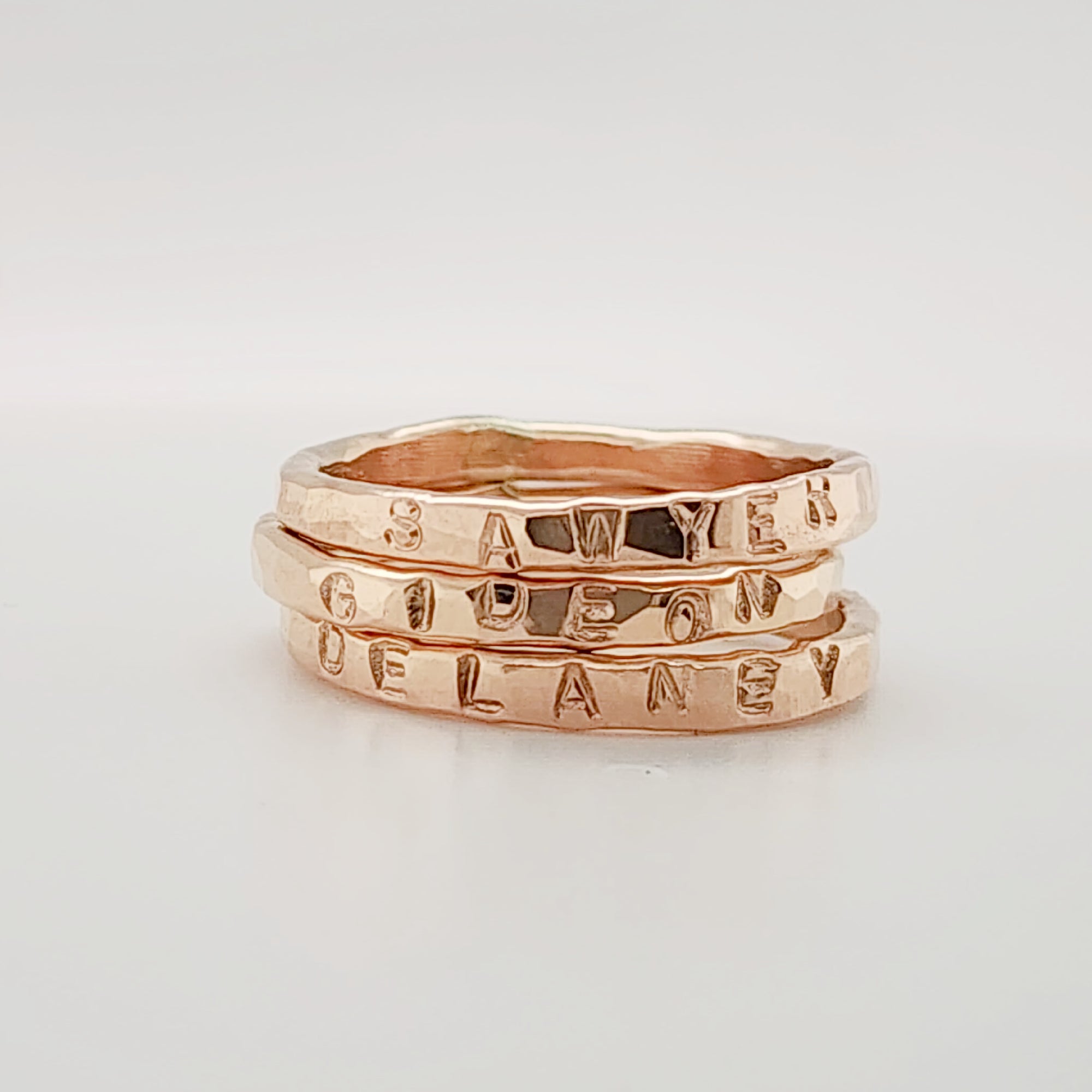 three handmade stacking rings stacked together and personalized with 'SAWYER', 'GIDEON', and 'DELANEY'