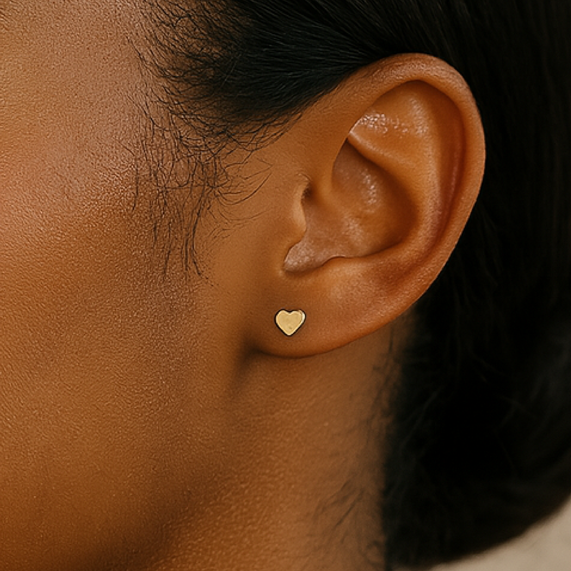Close-up of an ear wearing a gold heart-shaped earring.