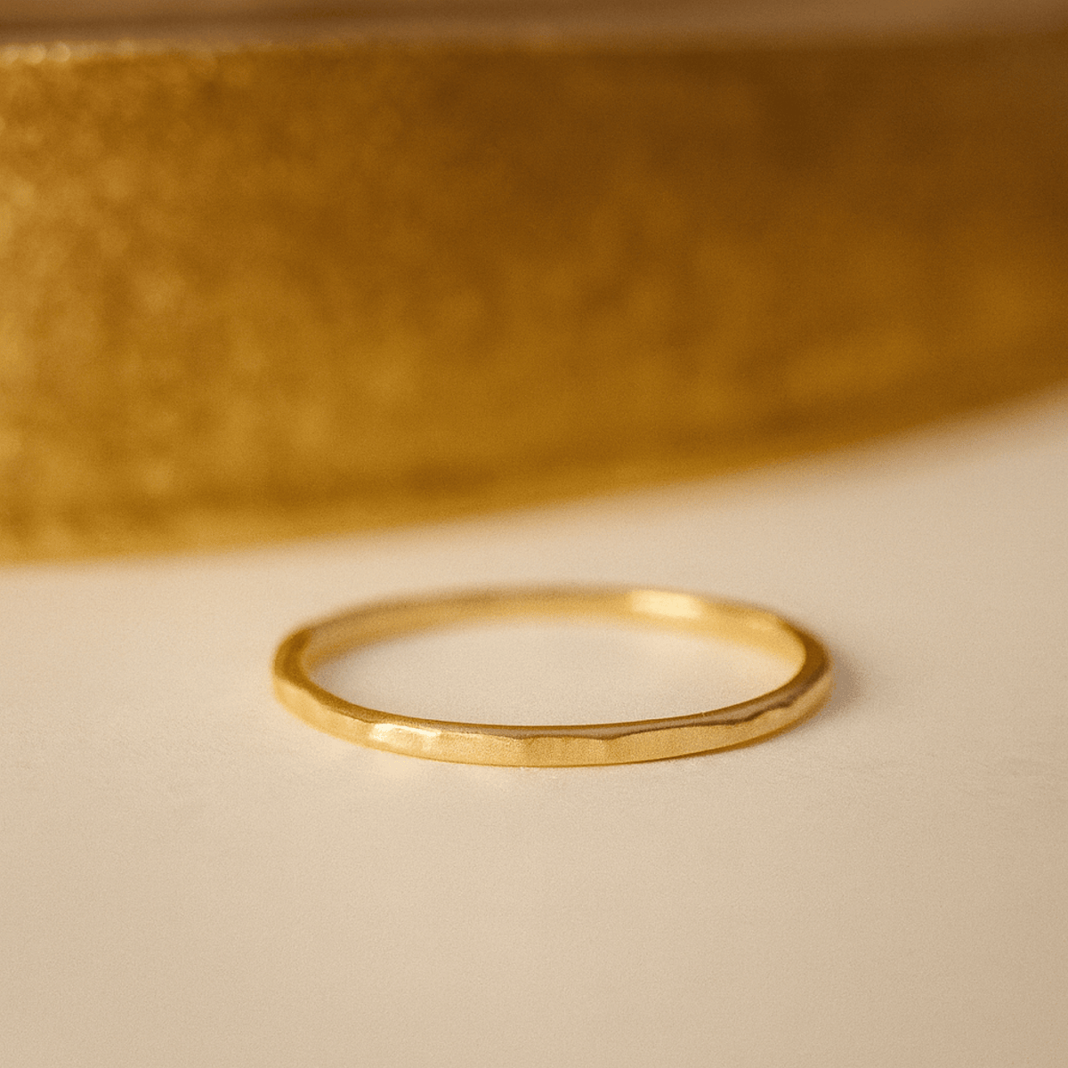 Gold ring on a beige surface with a blurred gold object in the background