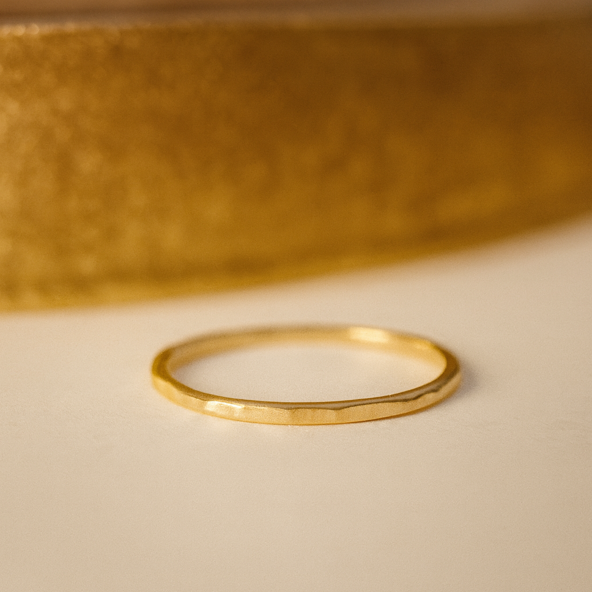 Gold ring on a beige surface with a blurred gold object in the background