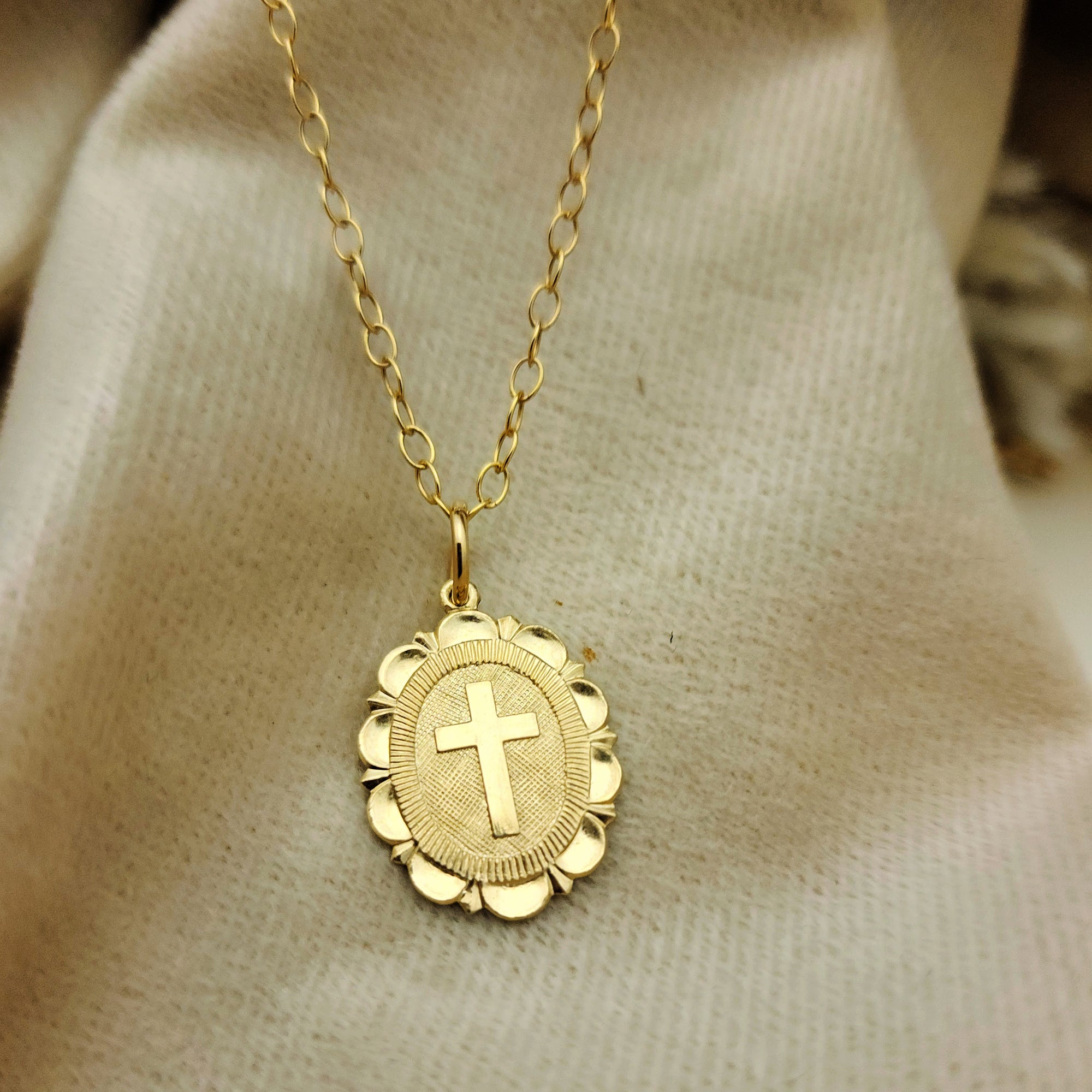 Gold necklace with a cross pendant on a beige fabric background