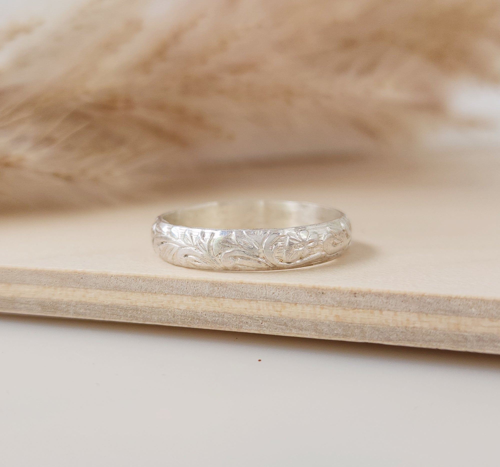 A sterling silver stacking ring with a floral pattern, displayed on a wooden surface.
