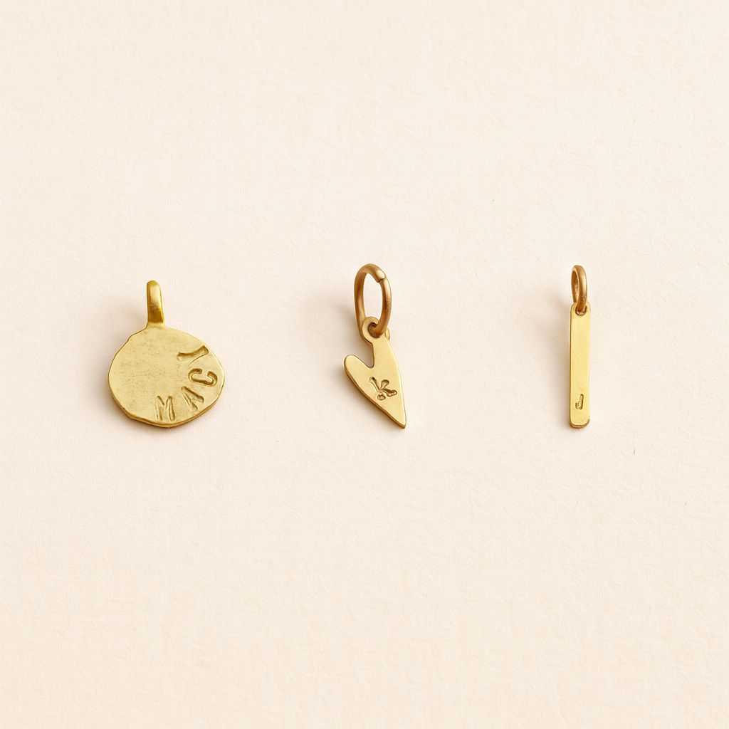 Three hand-stamped gold charms on a beige background
