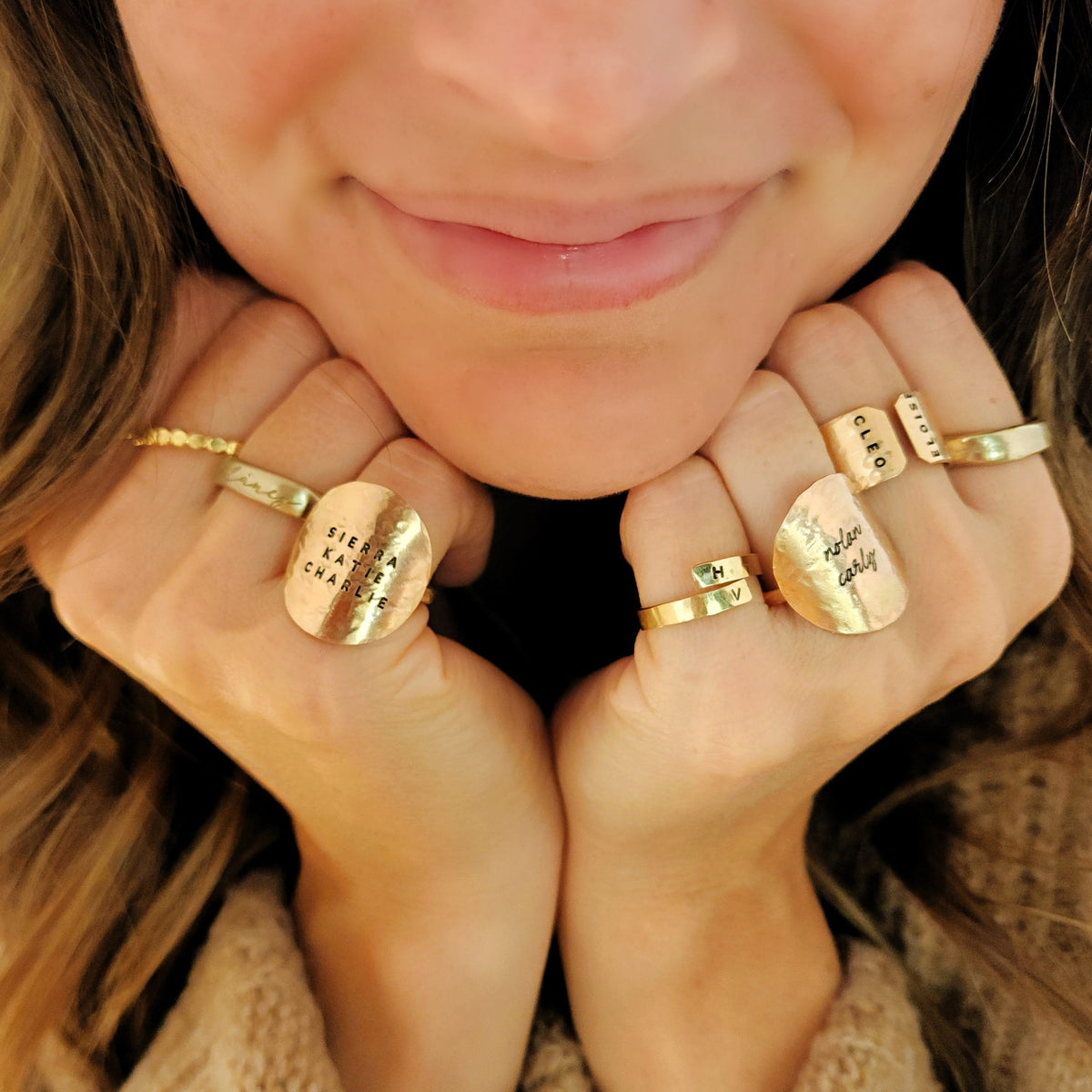 Woman smiling and wearing handcrafted gold name rings stacked together by Going Golden