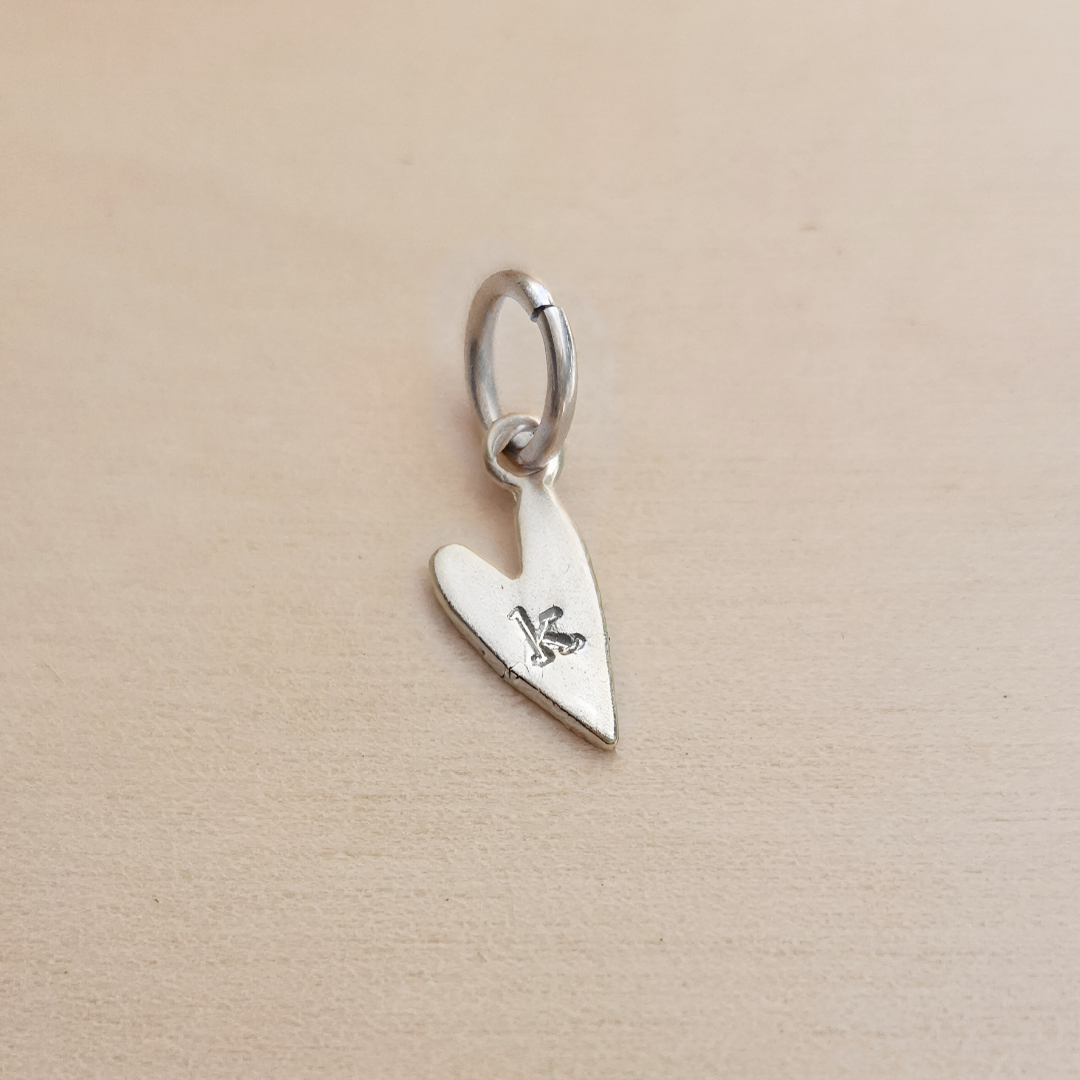 Silver heart-shaped pendant with a letter &#39;K&#39; on a beige background